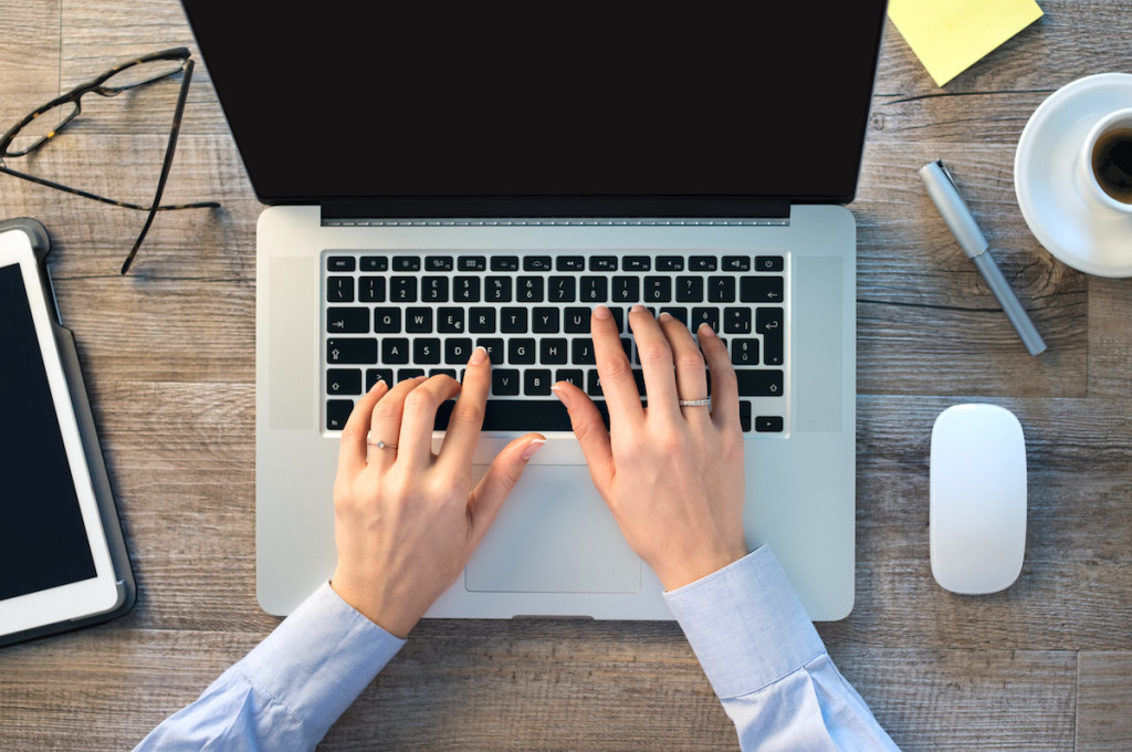 Closeup shot of a woman hand typing on keypad of her laptop. Girl is working in office at computer. Focus on typing on keypad of laptop.